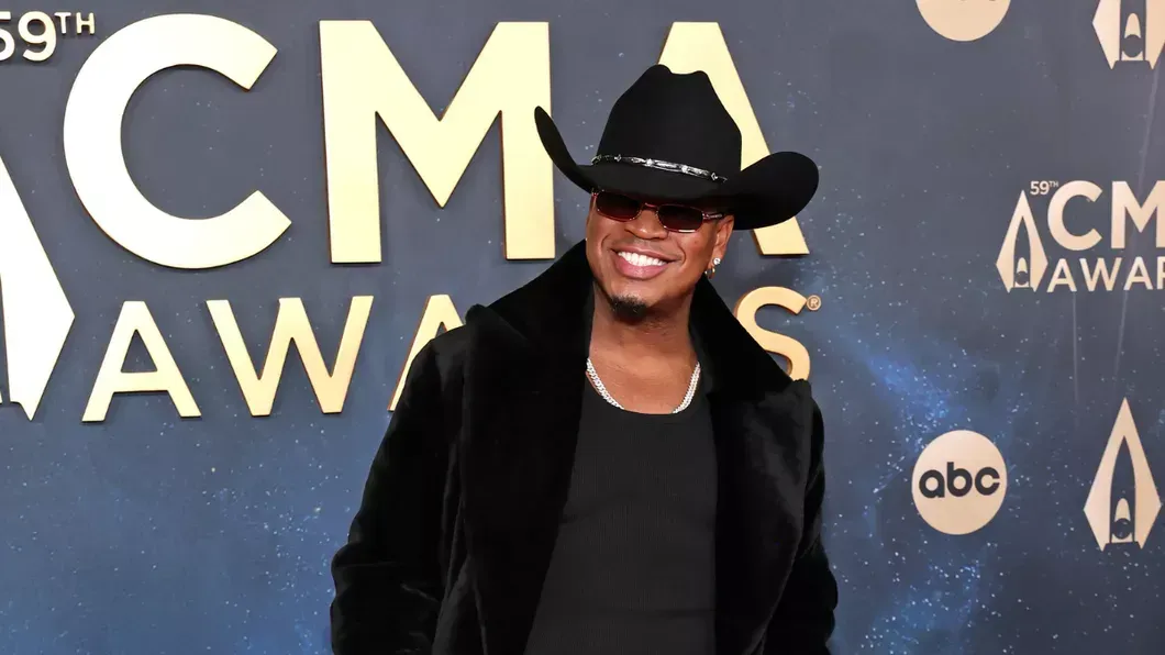 Person in black cowboy hat and jacket smiling on the ACM Awards red carpet.