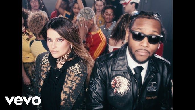Two performers pose in front of a crowded party scene, with a Vevo logo in the corner.