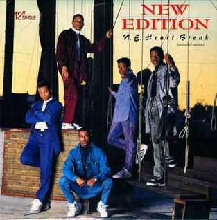 Five men in colorful outfits pose in front of a storefront with the sign “New Edition”