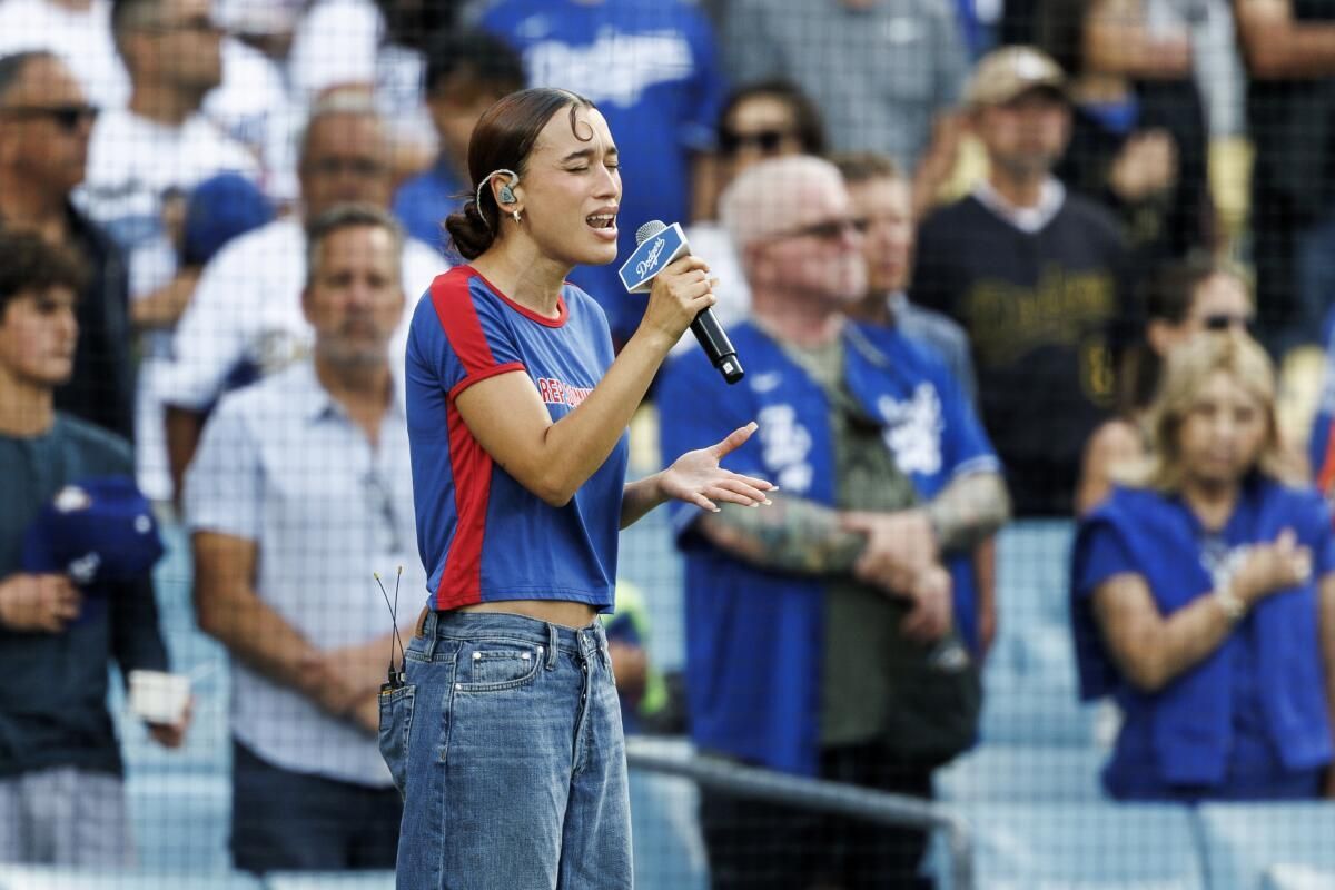 Singer in a blue and red shirt performing with a microphone before a crowd in a stadium