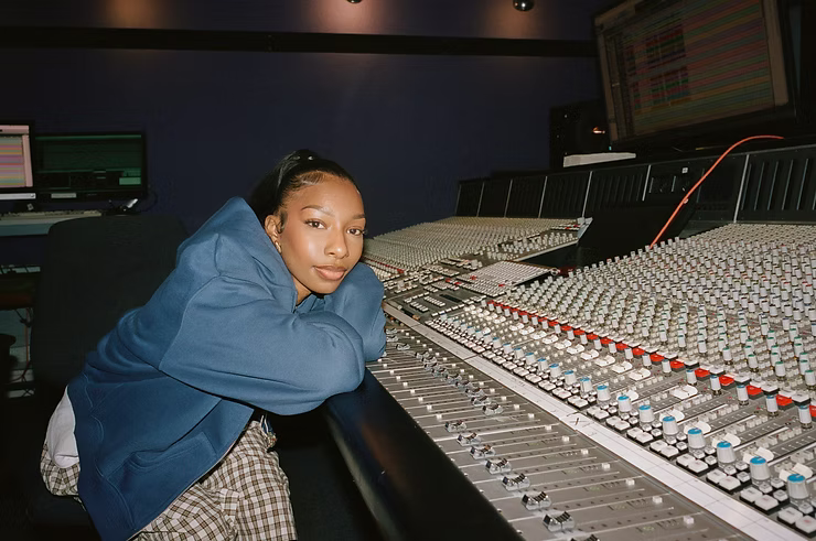 Person leaning on a large audio mixing console in a dim recording studio