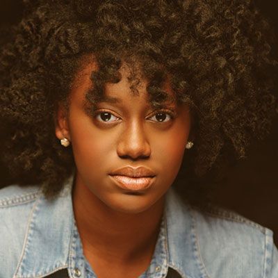 Portrait of a person with curly hair wearing a denim jacket, looking directly at the camera.