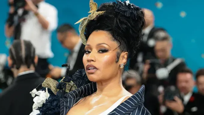 Woman in a black pinstripe outfit at a red carpet event, with photographers blurred in the background.