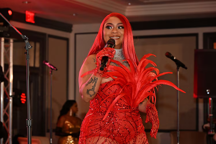 Woman in a bright pink coat at a formal event, walking past photographers and attendees.