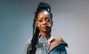 Stylish person in a denim jacket and glasses posing against a gray background