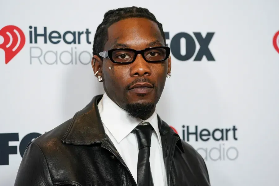 Man in black suit, tie, and leather jacket posing at an iHeartRadio FOX event backdrop
