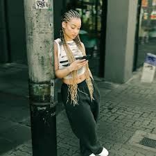 Person leaning against a pole while looking at a phone on a city sidewalk, wearing a striped top and black pants