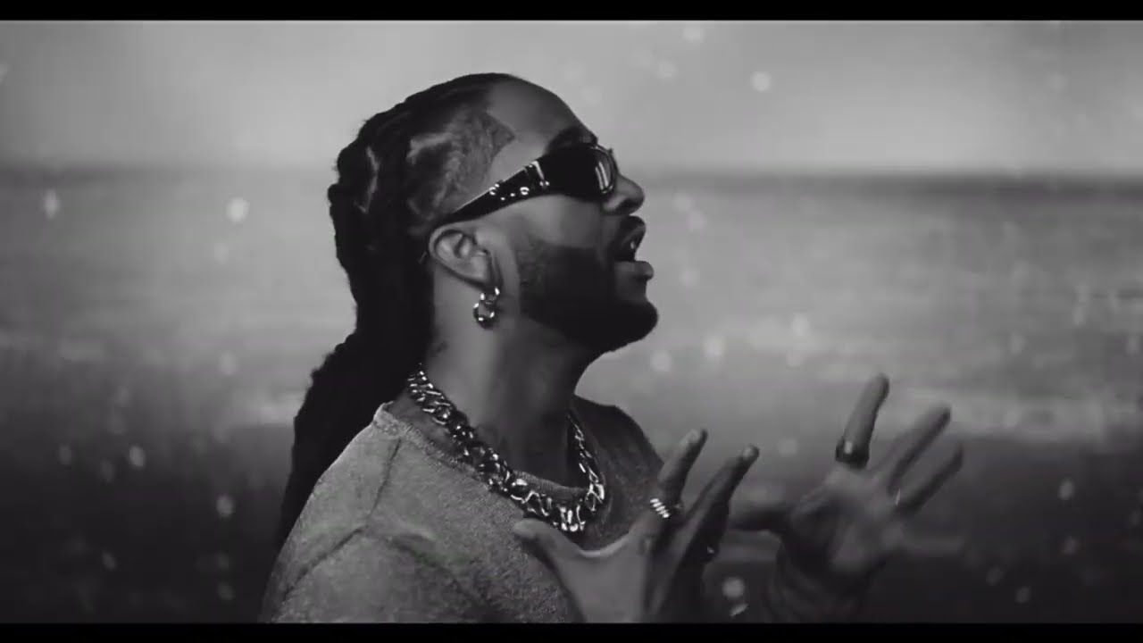 Black-and-white profile of a person singing with hands raised, wearing sunglasses and jewelry, against a blurred background