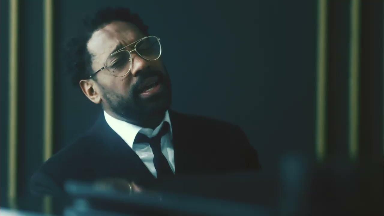 Man in glasses and dark suit speaking in a dimly lit room