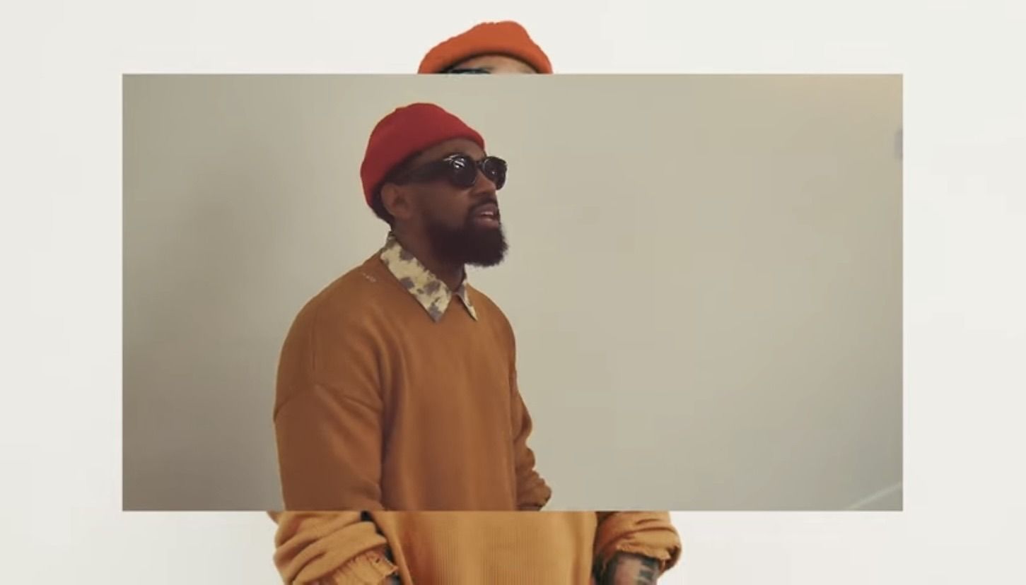 Person in a red hat and sunglasses standing against a plain beige wall.