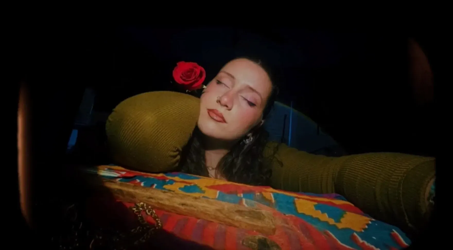 Person sleeping with a red rose near their face, resting on a colorful patterned cushion.