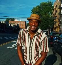 Smiling person in a striped shirt and straw hat standing on a sunny city street