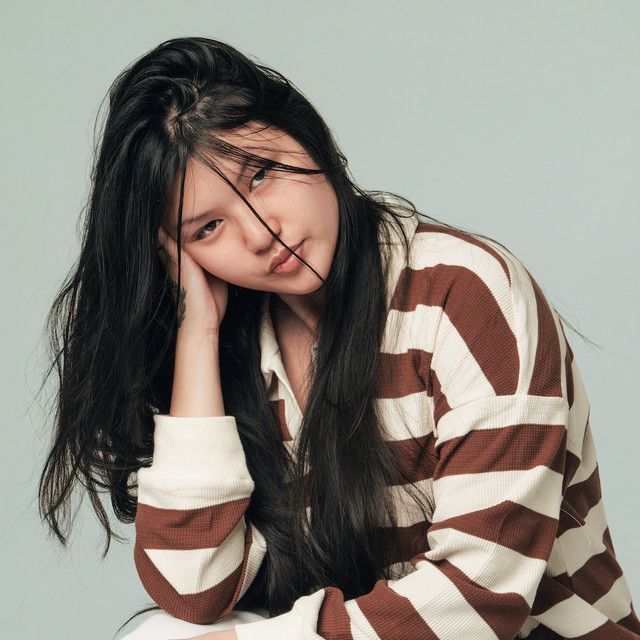 Young person with long dark hair resting their head on one hand, wearing a brown-and-white striped sweater.