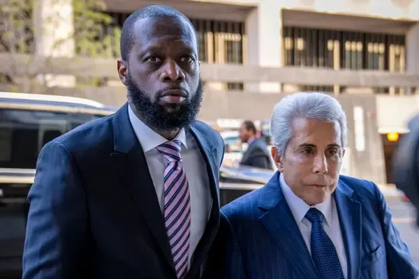 Two men in suits walking outside a building, one in a blue pinstripe suit and one in a dark suit with a striped tie.