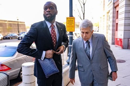 Two men in suits walk on a city sidewalk, one carrying a blue patterned bag.