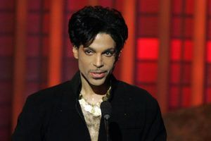 Person in a black jacket speaking at a microphone on a red-lit stage