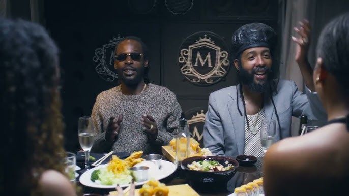 Two smiling people seated at a candlelit dinner table with drinks and food in a dark restaurant