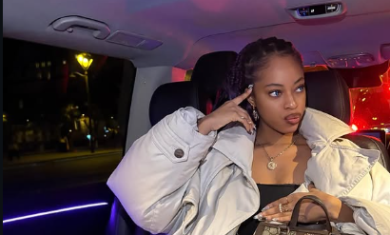 Woman in a white jacket sitting in a car at night, holding a phone and looking to the side.