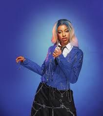 Person in a blue jacket and black skirt points at the camera against a blue backdrop.