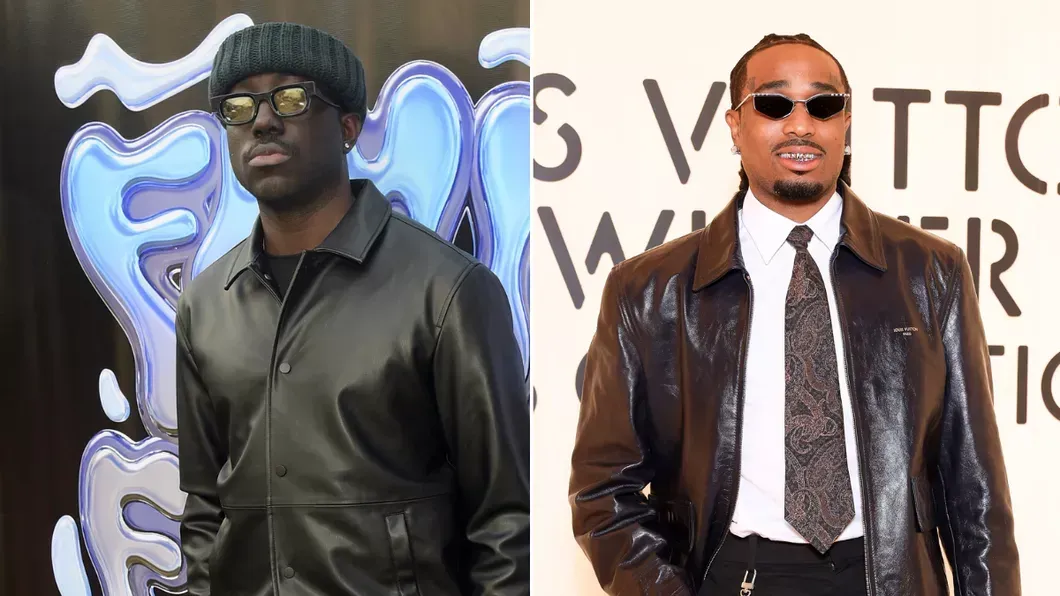 Two men posing at a red carpet event, one in a black jacket and glasses, the other in a brown suit and sunglasses.