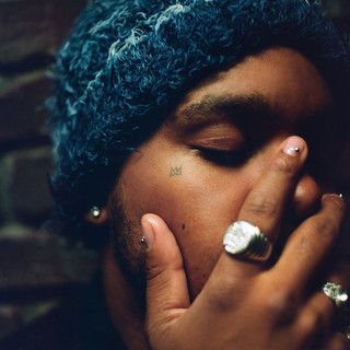 Close-up of a person with eyes closed, covering their mouth with a hand, wearing a knit hat and rings.