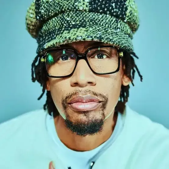 Close-up portrait of a person wearing glasses and a green knit hat against a light blue background