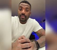 Man in white shirt leaning toward the camera indoors, with blue lighting in the background.