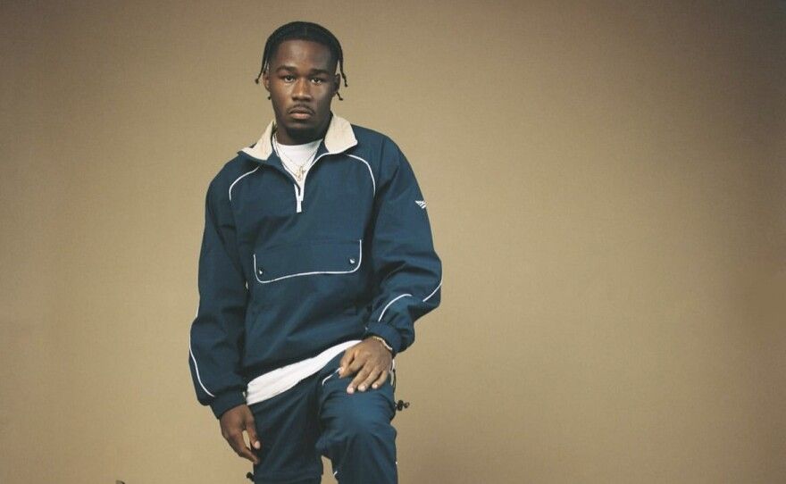 A man in a blue tracksuit poses against a plain beige background.