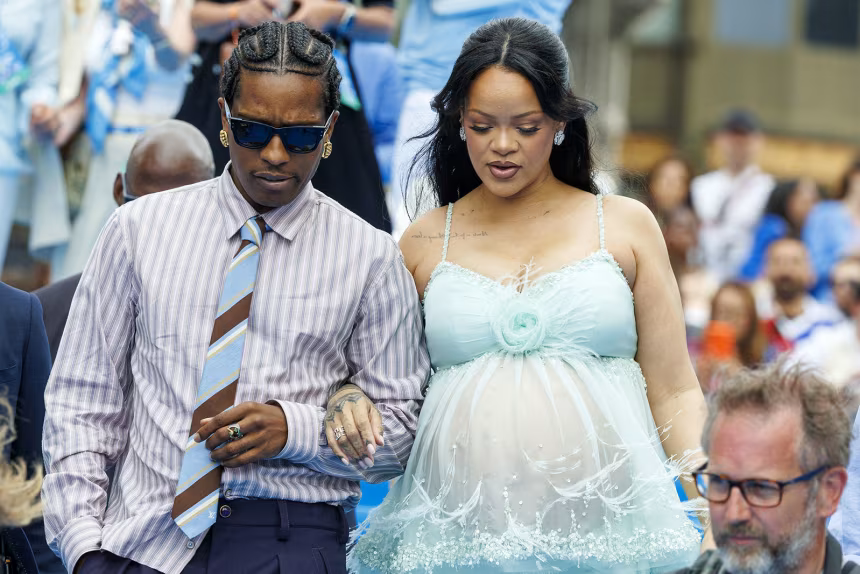 A man in a striped shirt and tie walks beside a woman in a light blue dress at an outdoor event.