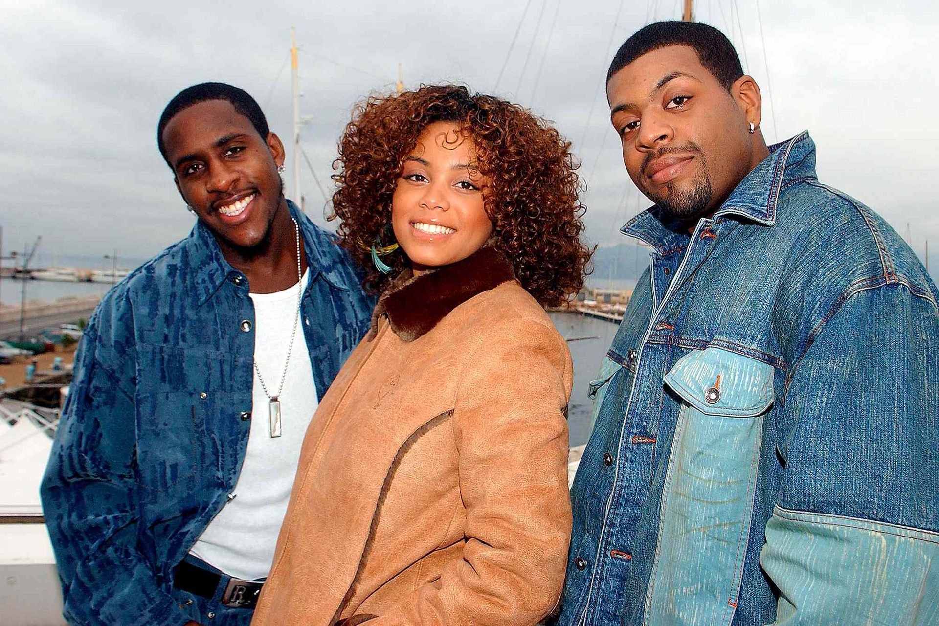 Three smiling people in denim and tan jackets posing outdoors in a snowy setting
