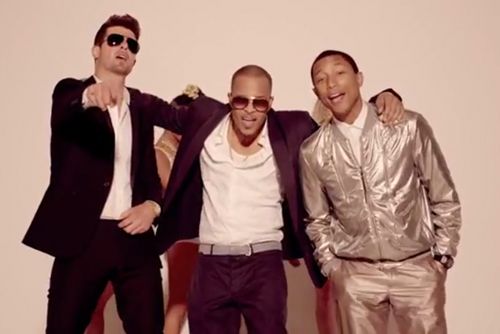 Three men posing together, smiling, in dark and metallic outfits against a plain background.