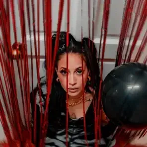 Woman behind red strings, staring at camera with a black balloon beside her.