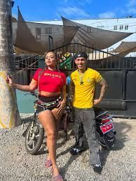 Two people posing with scooters in front of a building under a blue sky