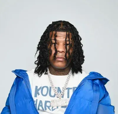 Studio portrait of a person in a blue jacket and white shirt, wearing gold chains, against a light background