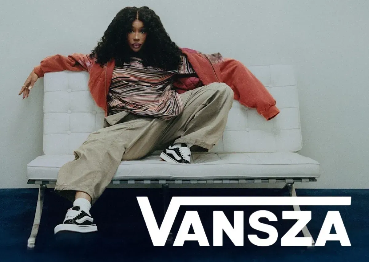 Person lounging on a white couch in red jacket and beige pants with “VANSZA” text below
