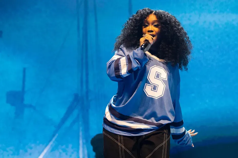 Singer performing on stage in a blue jersey under blue lighting, holding a microphone