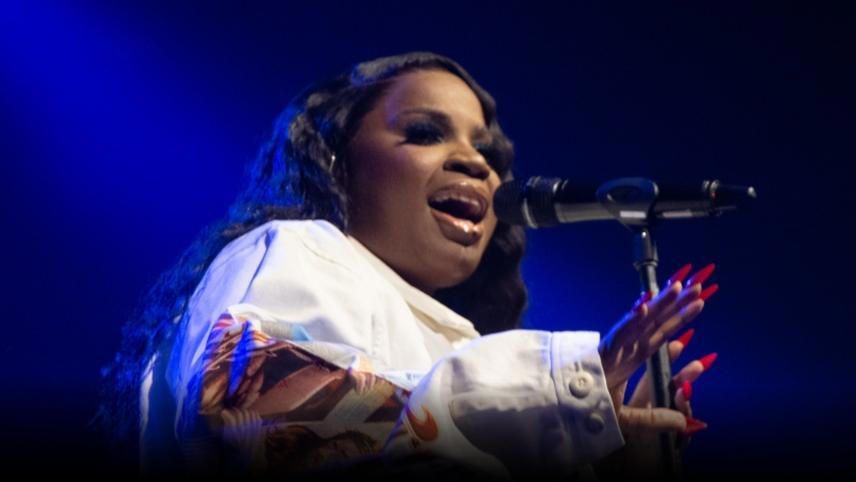 Singer performing onstage under blue lighting, singing into a microphone with expressive hand gestures.