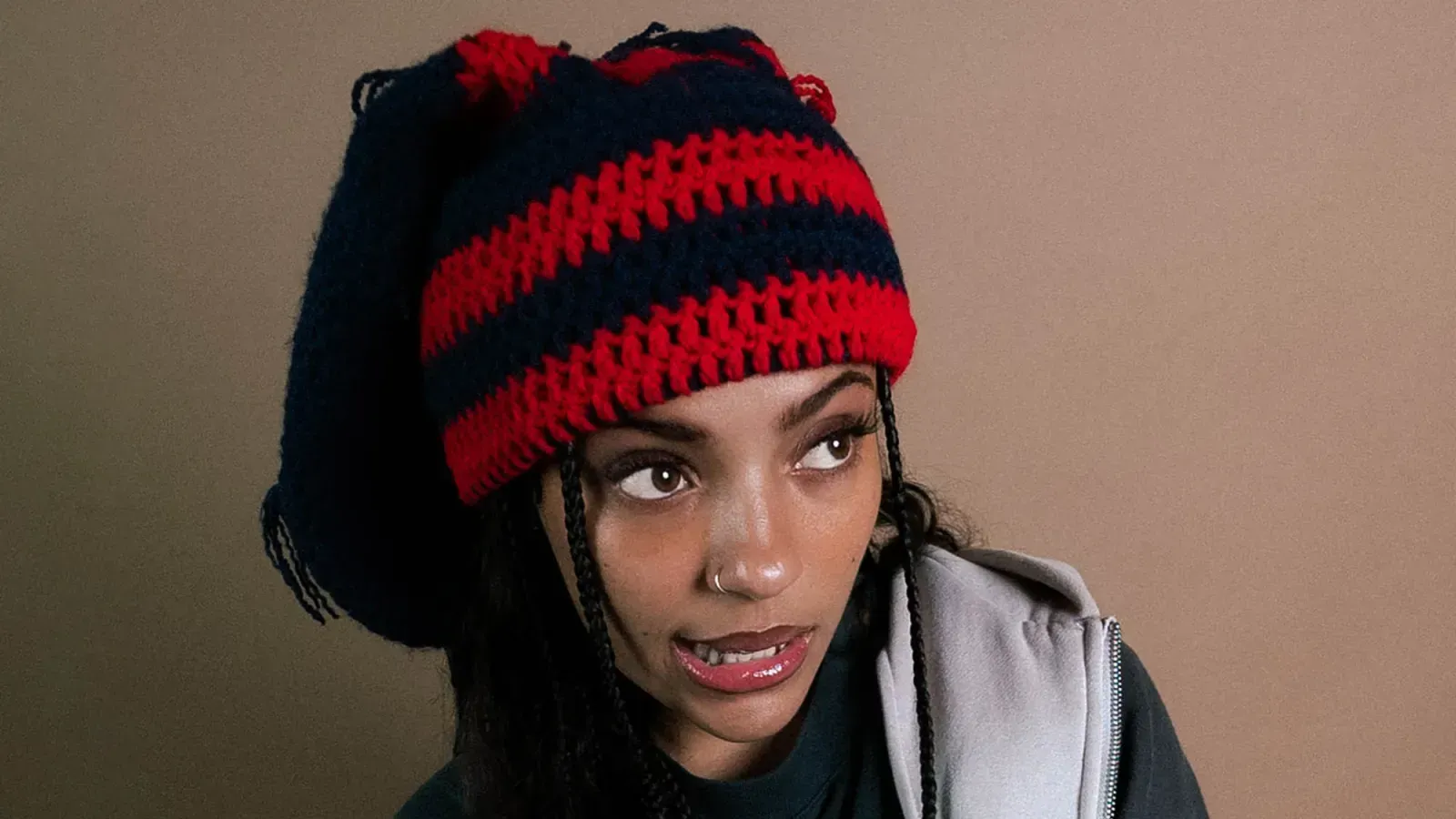 Person wearing a red-and-black knit hat, looking to the side against a plain beige background