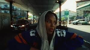 Person in a hoodie leaning under an overpass, with cars and city traffic in the background.