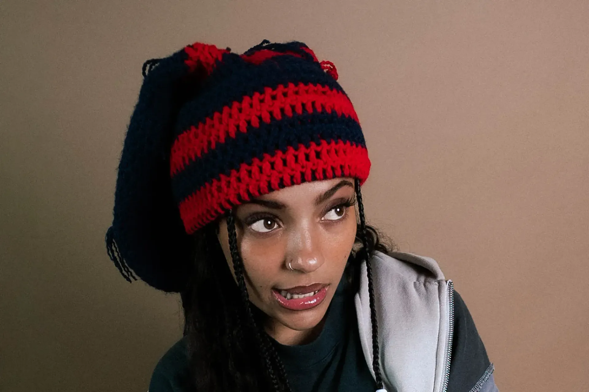 Person wearing a red-and-black striped knit hat and gray hoodie, looking to the side.