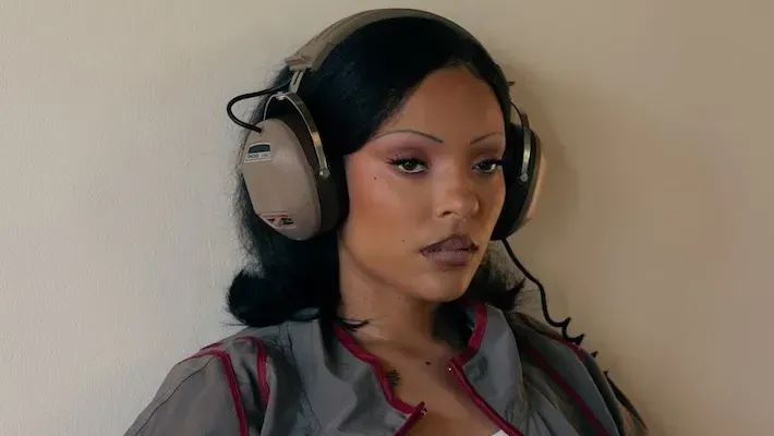 Woman wearing large headphones against a plain wall, looking off to the side with a neutral expression.