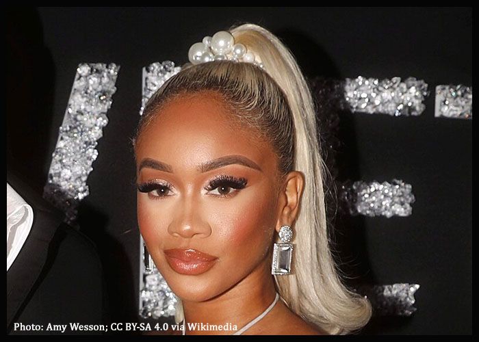Woman with platinum blonde ponytail and silver earrings posing against a black backdrop with glittering letters