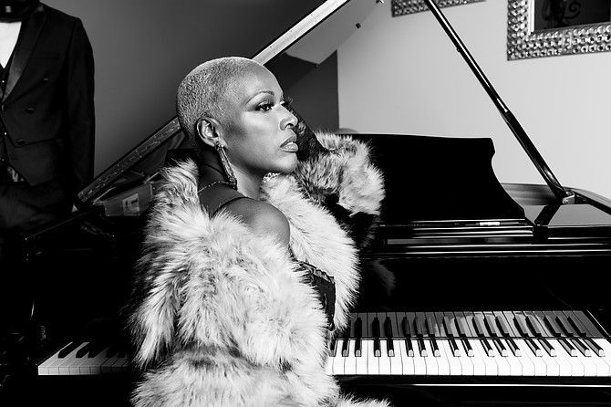 Person in a fur coat seated at a piano, in black-and-white.