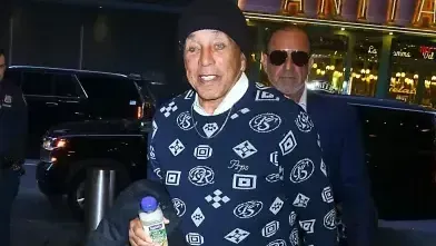 Two men in dark clothing walking at night, one smiling and holding a water bottle.