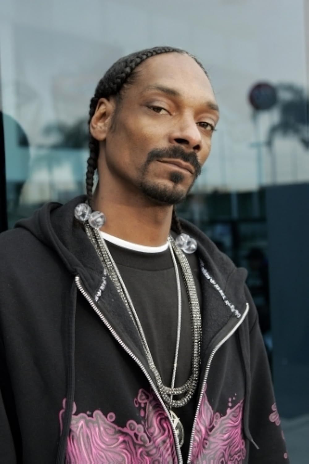 Person with braided hair and goatee wearing a black jacket with pink details, standing outdoors.