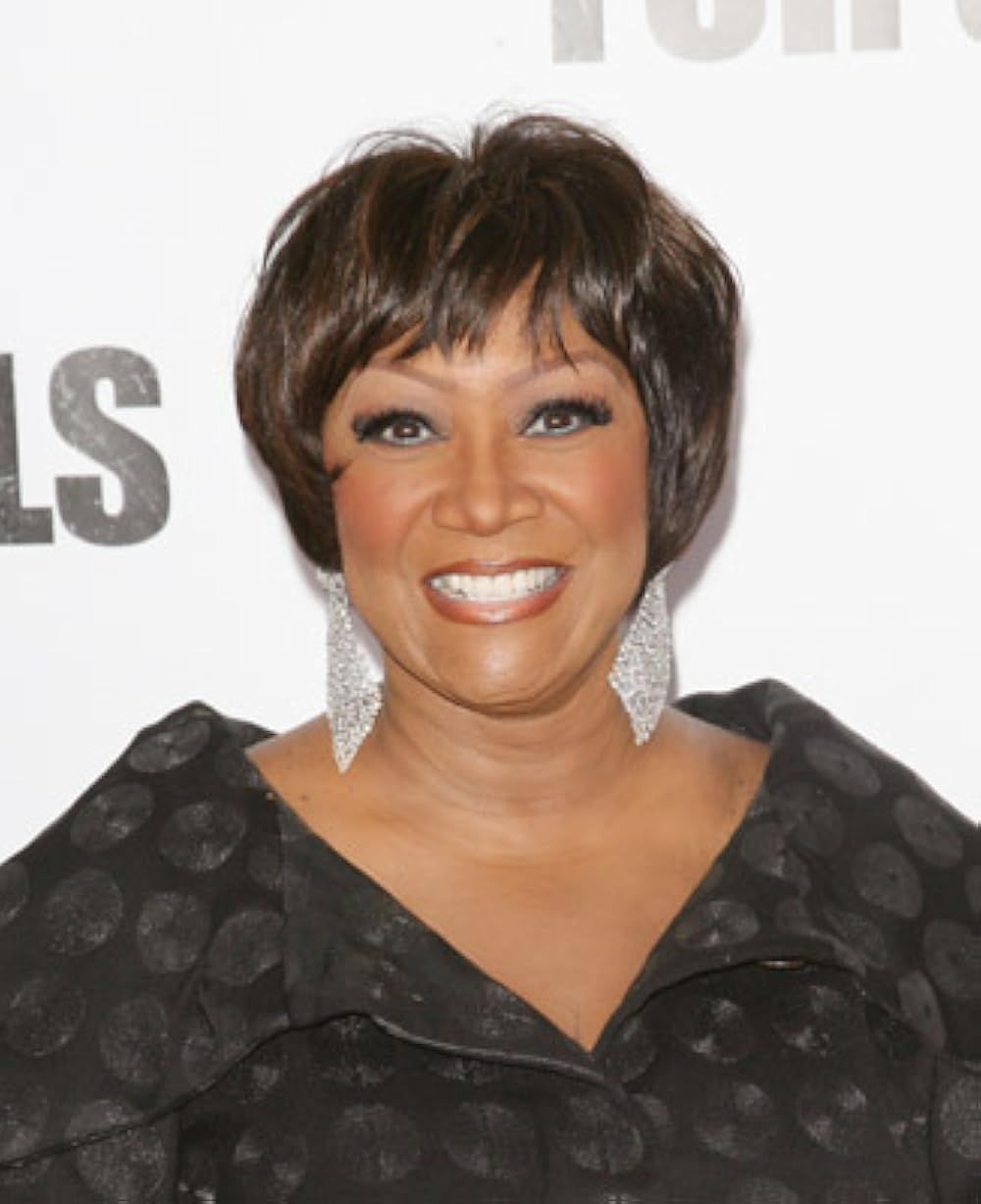 Smiling woman in black patterned dress with large earrings at a red carpet event