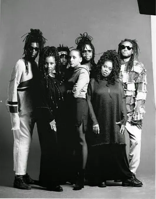 Five people pose in a studio, dressed in dark and light clothing.