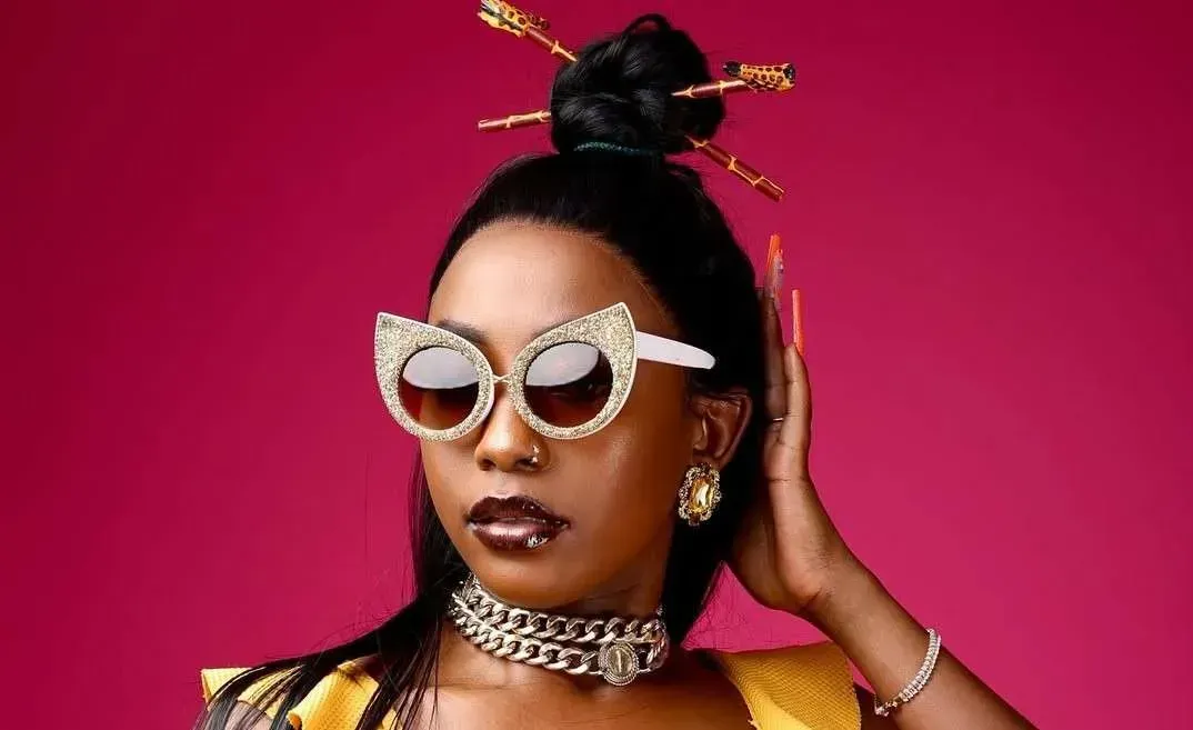 Portrait of a person in jeweled sunglasses and gold jewelry against a bright pink background
