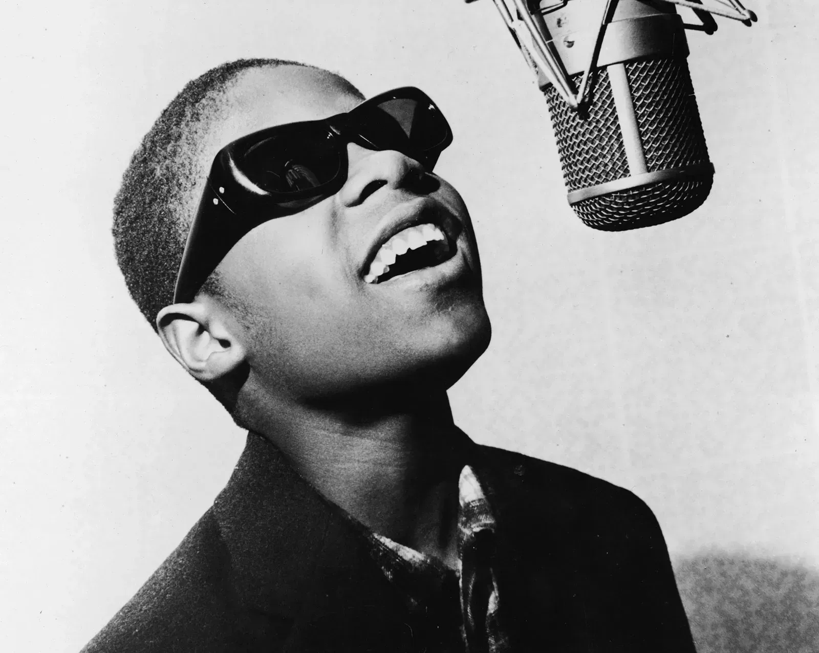 Person in sunglasses singing into a microphone, mouth open in black-and-white.