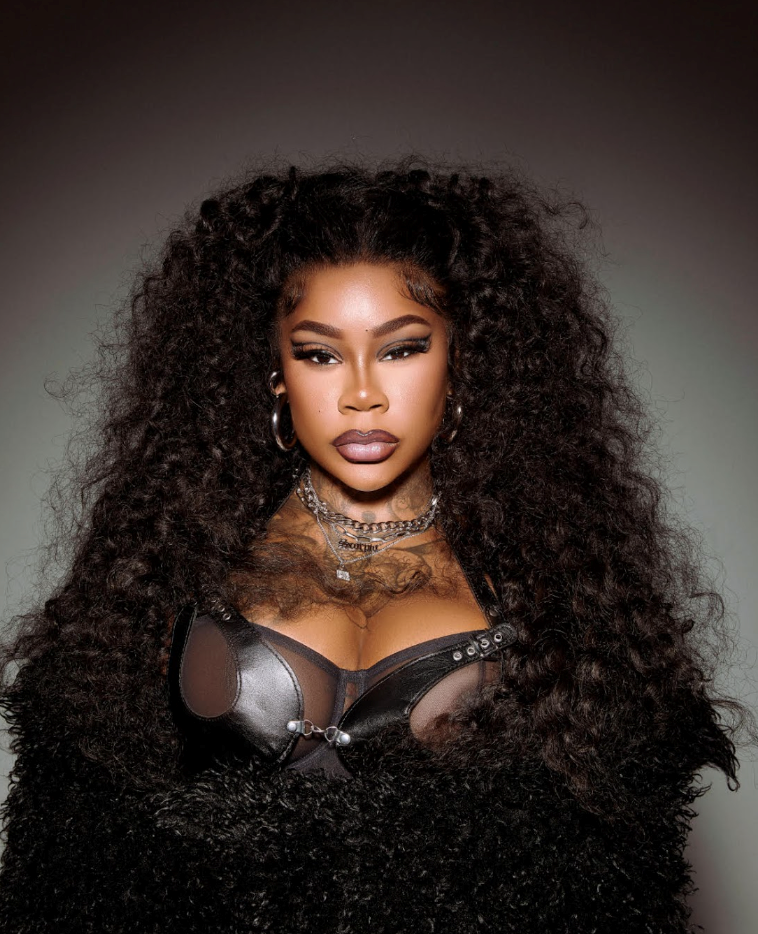 Woman with long curly black hair in a black corset and choker against a dark background